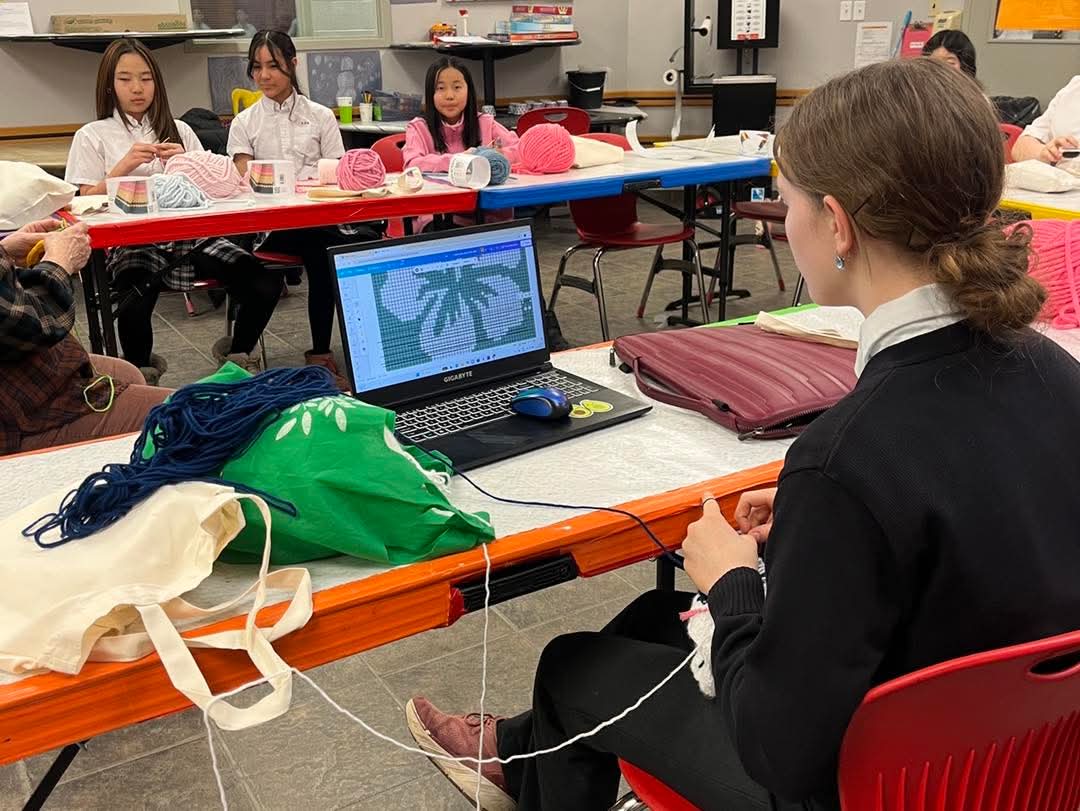 Students knitting and crocheting with a laptop showing a pattern design