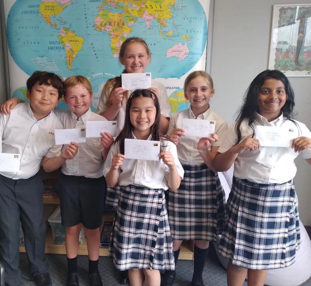 Students holding addressed envelopes in front of a world map