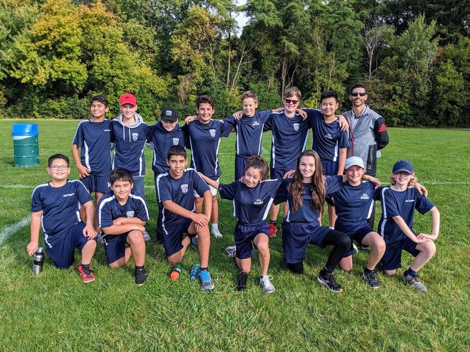 APA soccer All Stars team in navy uniforms with coach on a grass field